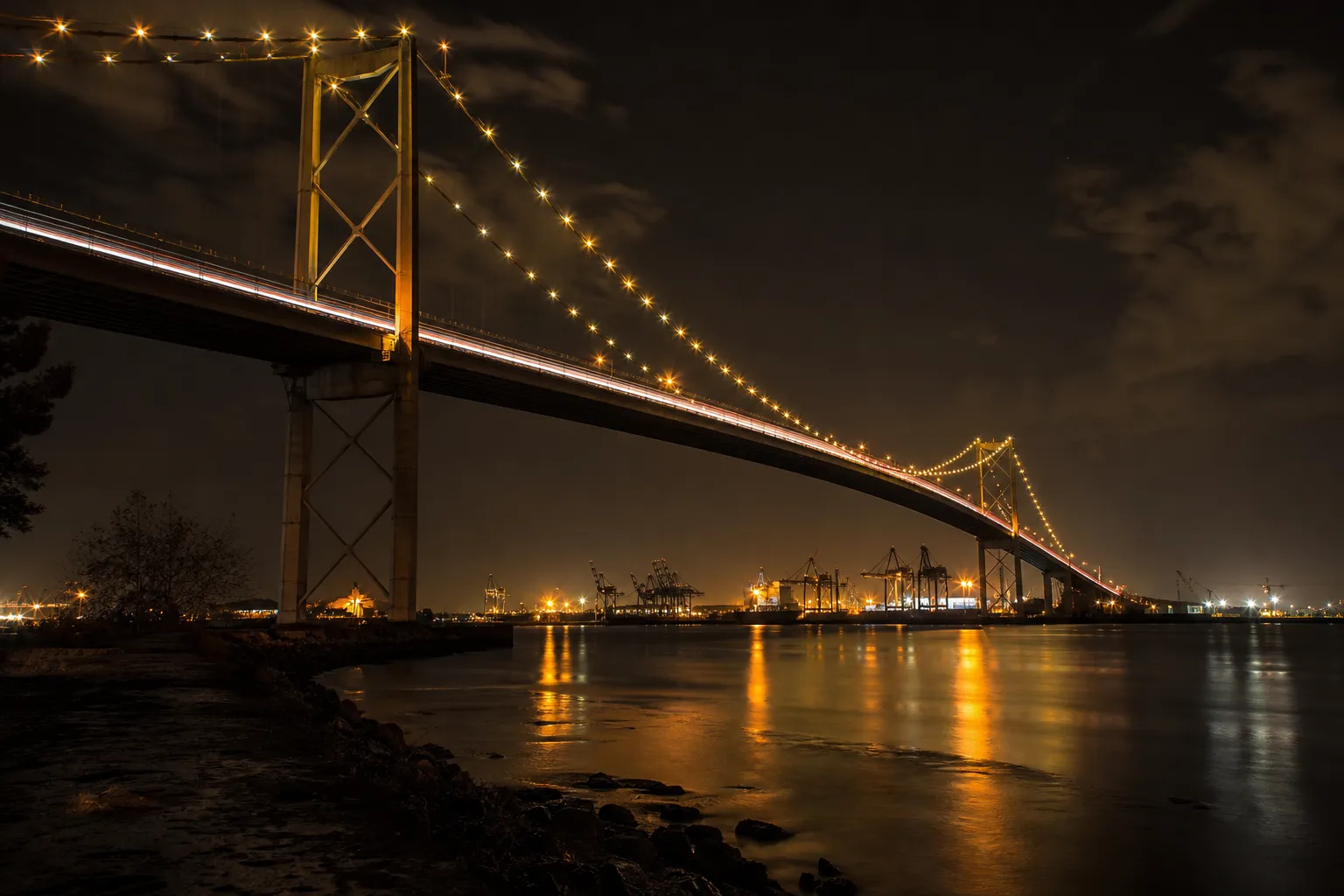 Suspension bridge at night with port cranes in the distance